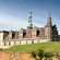 An enormous Renaissance castle with a tall spire in the middle of its roof, at the edge of an embankment